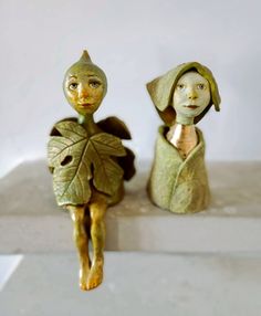 two ceramic figurines sitting on top of a white table next to each other