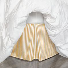 a bed with white sheets and yellow striped bedskirt under a comforter on the floor