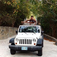 a man is standing on top of a jeep in the driveway with his arms outstretched