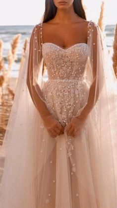 a woman in a wedding dress standing on the beach with her arms behind her back