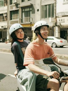 a man and woman riding on the back of a scooter down a street