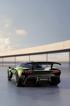 a green and black sports car is parked in front of a concrete wall with a bridge behind it