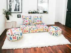 a brightly colored couch and ottoman in a white room with wooden floors, framed pictures on the wall