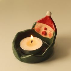 a small candle holder with a santa hat on it's head and a lit candle in the middle