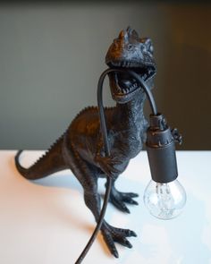 a toy dinosaur holding a light bulb on top of a table