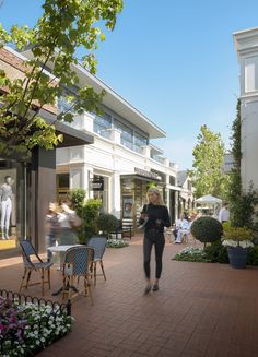 a woman is walking down the sidewalk in front of some shops and people sitting at tables