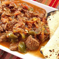 a white plate topped with meat and green peppers next to two tortilla bread