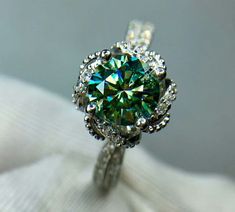 a green diamond ring sitting on top of a white cloth