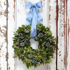 a wreath hanging on the side of a white wooden door with a blue ribbon tied around it