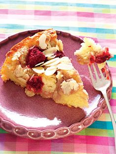 a piece of pie with raspberries and almonds on a pink plate next to a fork