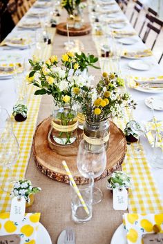 the table is set with yellow and white flowers in mason jar vases on wood slices