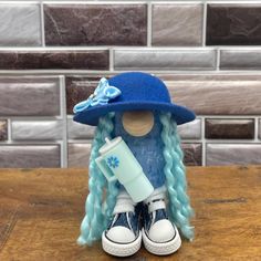 a doll with blue hair wearing a hat and holding a cup on top of a wooden table