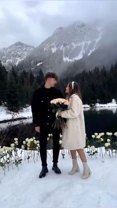 a man standing next to a woman holding flowers in front of a snow covered mountain