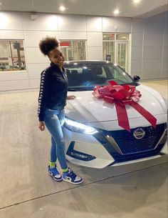 a woman standing next to a white car with a red bow on it's hood