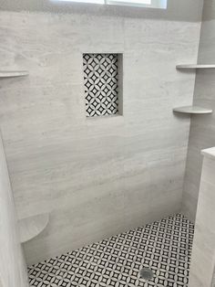 a white bathroom with black and white tiles on the shower wall, flooring and shelves