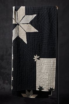 a black and white quilt hanging from a metal pole on a dark background with leaves