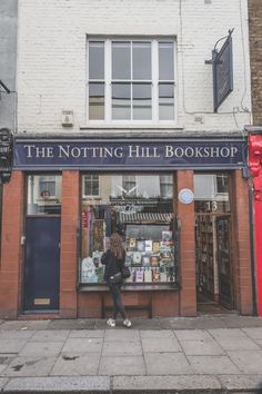 a person sitting on a bench in front of a book shop with the words, the notting hill bookshop