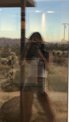 a woman taking a selfie in front of a window with the desert behind her