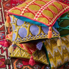 three colorful pillows stacked on top of each other in front of a rug with tassels