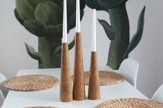 three wooden candlesticks sitting on top of a white table next to a plant