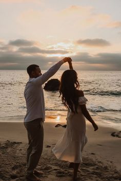 a man and woman dancing on the beach at sunset with their arms in the air