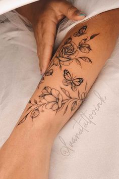 a woman's arm with flowers and butterflies on it, sitting on a bed