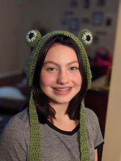 a woman wearing a green knitted hat with eyes on it's head and smiling