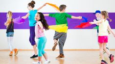 group of children dancing on the floor with their arms in the air and colorful streamers behind them