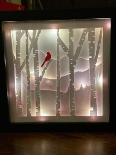 a red bird sitting on top of a tree filled forest under a light up shadow box