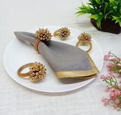 a white plate topped with gold jewelry on top of a table next to a potted plant