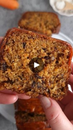 a person holding a piece of bread with raisins on it and carrots in the background