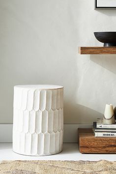 a white vase sitting on top of a wooden table next to a bowl and books