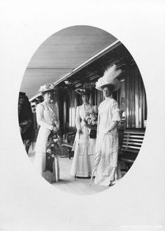 three women in dresses and hats standing on a train platform