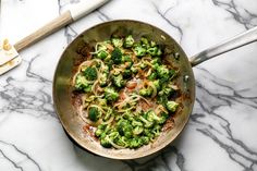 a pan filled with noodles and broccoli on top of a marble countertop