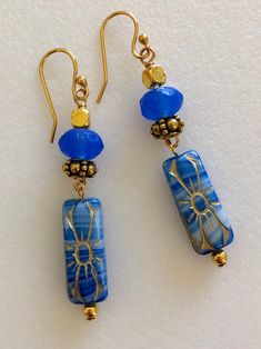 "Beautiful marbled blue denim Czech flower beads accented with golden bronze. 20 x 8 mm pressed glass rectangles. Topped with cornflower blue Czech sea glass beads. 8 x 6 mm matte blue rondelles. Ornate antique gold beaded spacers and cube accents. Gold plated French ear hooks. Total drop 2\"." Bohemian Blue Earrings With Gold Beads, Artisan Blue Beaded Earrings As Gift, Blue Earrings With Spacer Beads For Gift, Artisan Blue Jewelry With Gold Beads, Artisan Blue Beaded Earrings, Copper Jewelry Diy, Czech Beads Jewelry, Denim Earrings, Czech Glass Jewelry