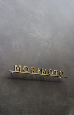 the word mormoto is written in gold on a gray surface with a small toothpick