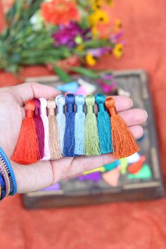 a hand holding a row of tassels with flowers in the background