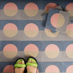 a woman's feet with green sandals standing in front of a patterned wallpaper