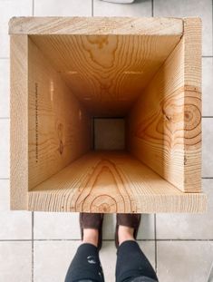 a person standing in front of a toilet with their feet on the floor holding a wooden box