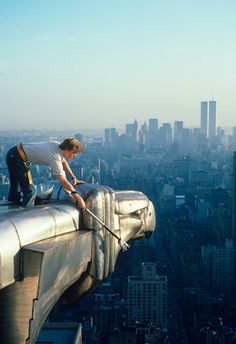 a man on top of a tall building cleaning the roof with a mop in new york city