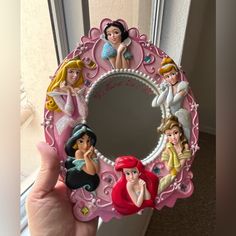 a hand holding up a pink mirror with disney princess pictures on the front and sides