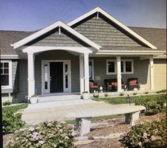 a gray house with white trim on the front door and porch, surrounded by shrubs and flowers