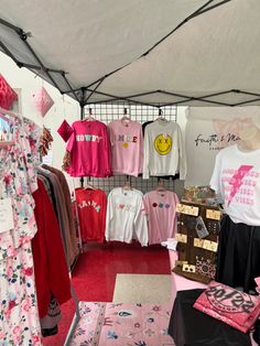 an open tent with clothing on display and other items in the area around it, including t - shirts