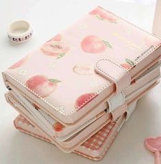 a stack of pink notebooks sitting on top of a table next to a cup