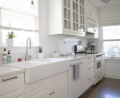 a kitchen with white cabinets and wood flooring next to a window in front of the sink