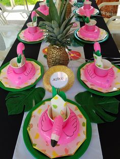 a table set up with pink flamingo plates and pineapple centerpieces for a party