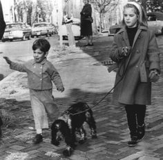 an old black and white photo of two children walking their dogs on a sidewalk in the winter