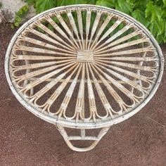 a white wicker table sitting on top of a dirt ground next to green plants