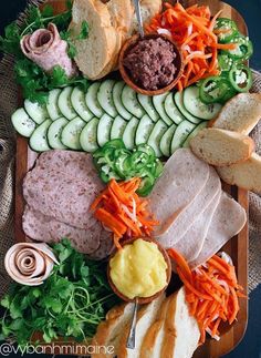 an assortment of meats and vegetables on a platter with bread, cucumbers, carrots, lettuce