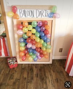 balloons are arranged in a wooden frame on the floor next to a sign that says balloon darts